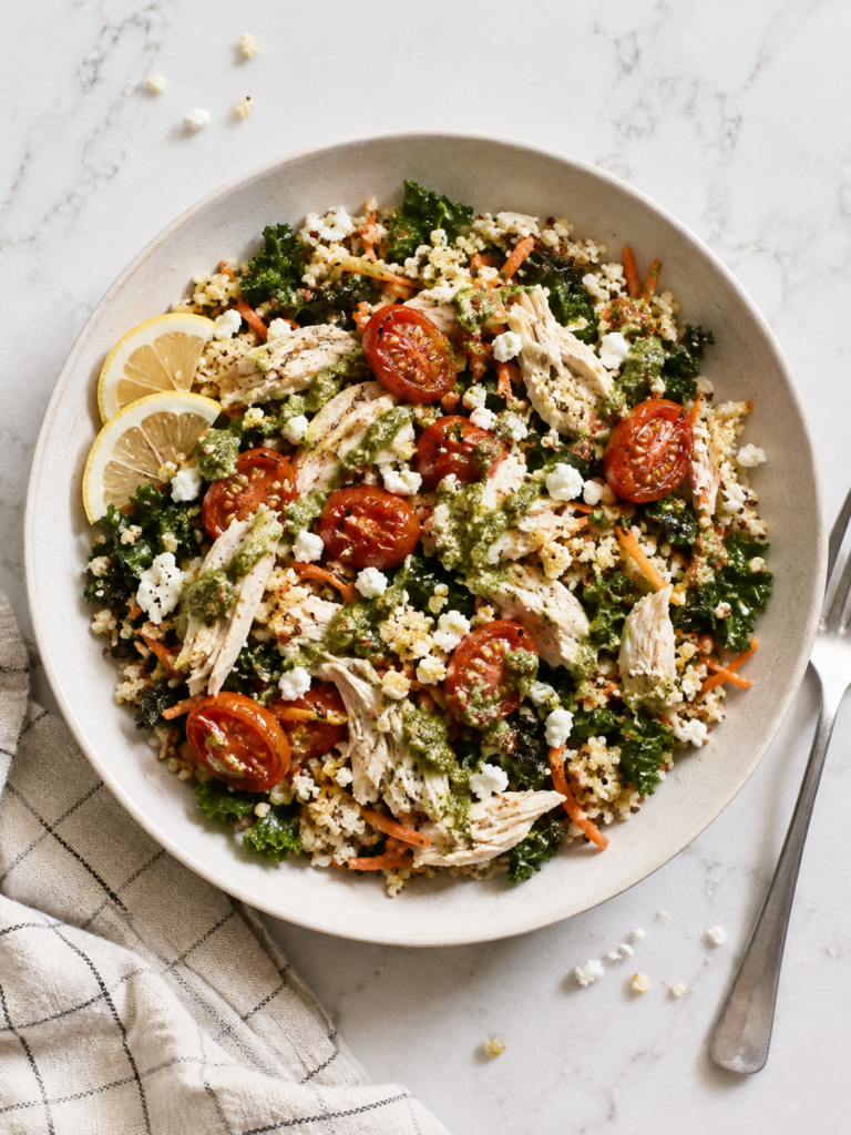 first watch copycat bowl of pesto chicken and quinoa with bright red roasted tomatoes, rotisserie shredded chicken, and greens, with lemon slices.