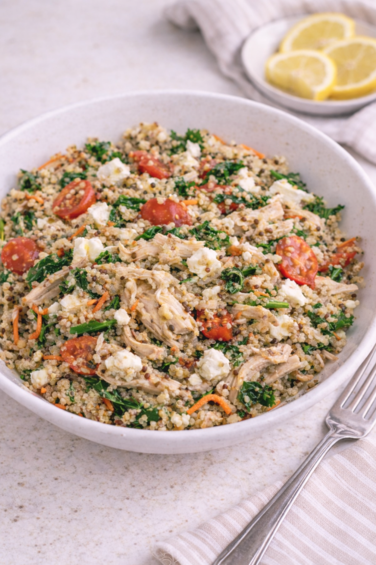 bowl of pesto chicken quinoa with bright red roasted tomatoes, rotisserie shredded chicken, and greens, next to plate of lemon slices.