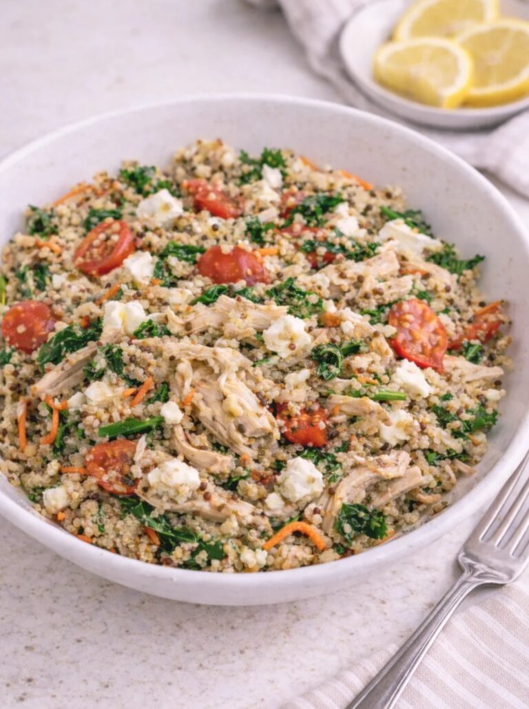 bowl of pesto chicken quinoa with bright red roasted tomatoes, rotisserie shredded chicken, and greens, next to plate of lemon slices.