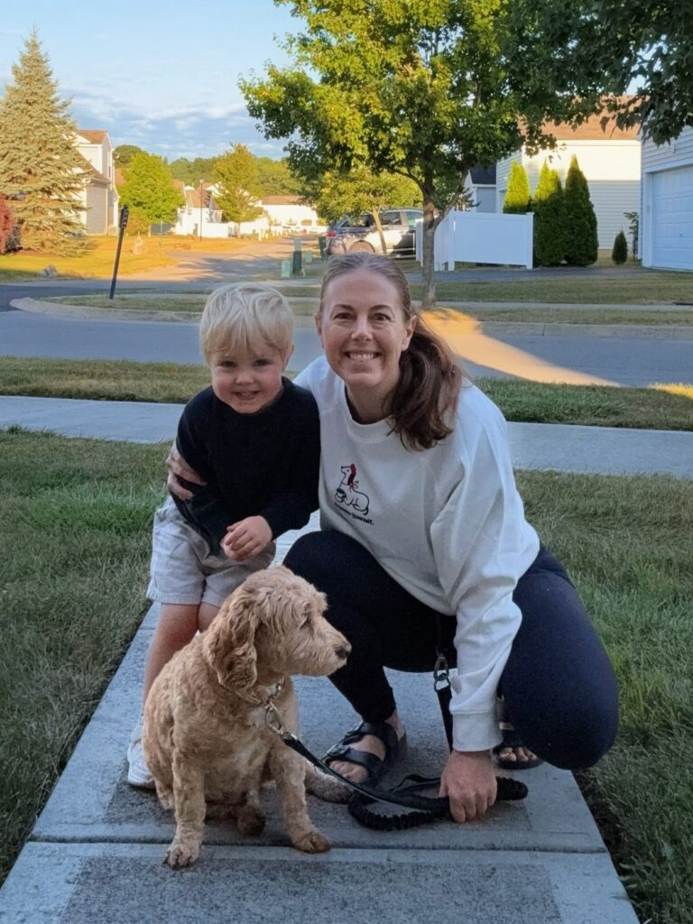Single mom kneeling on a sidewalk with her toddler son and dog during an evening walk in a suburban neighborhood.