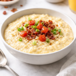 bowl of copycat another broken egg slow cooker grits topped with bacon, scallions, and tomato