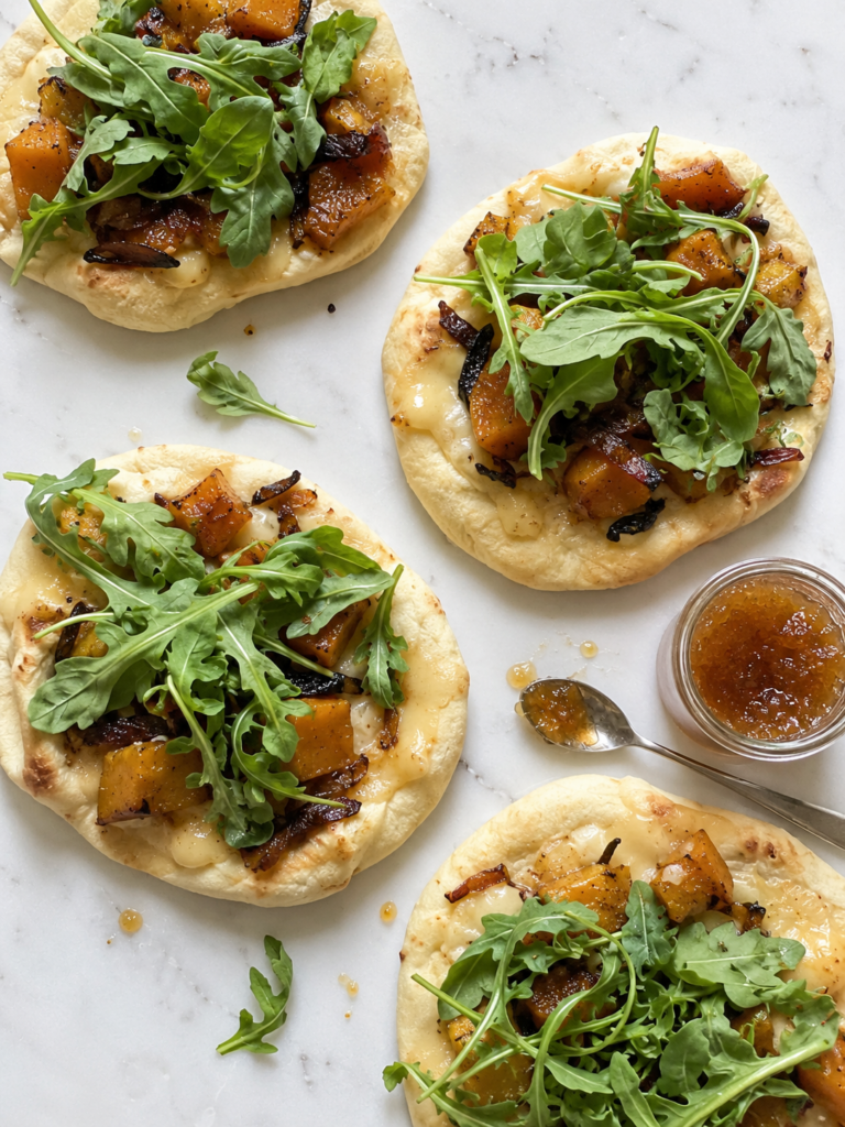 Four butternut squash flatbreads on marble with a jar of fig jam, shown from overhead