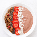 chocolate covered strawberry smoothie bowl topped with coconut flakes, strawberries, and dark chocolate granola