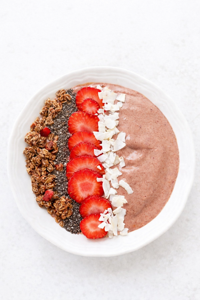 chocolate covered strawberry smoothie bowl topped with coconut flakes, strawberries, and dark chocolate granola