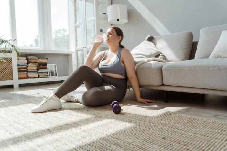 tired woman sitting on floor against her couch, recovering after a workout at home