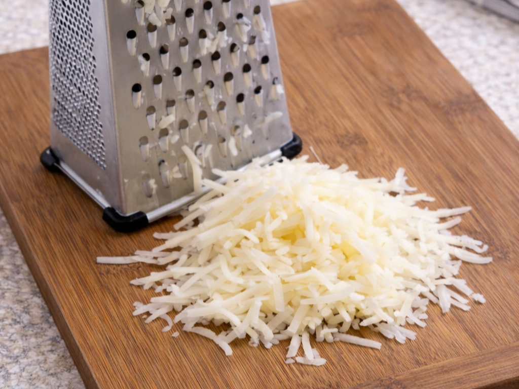 Grating russet potatoes on cutting board for extra crispy homemade hashbrowns