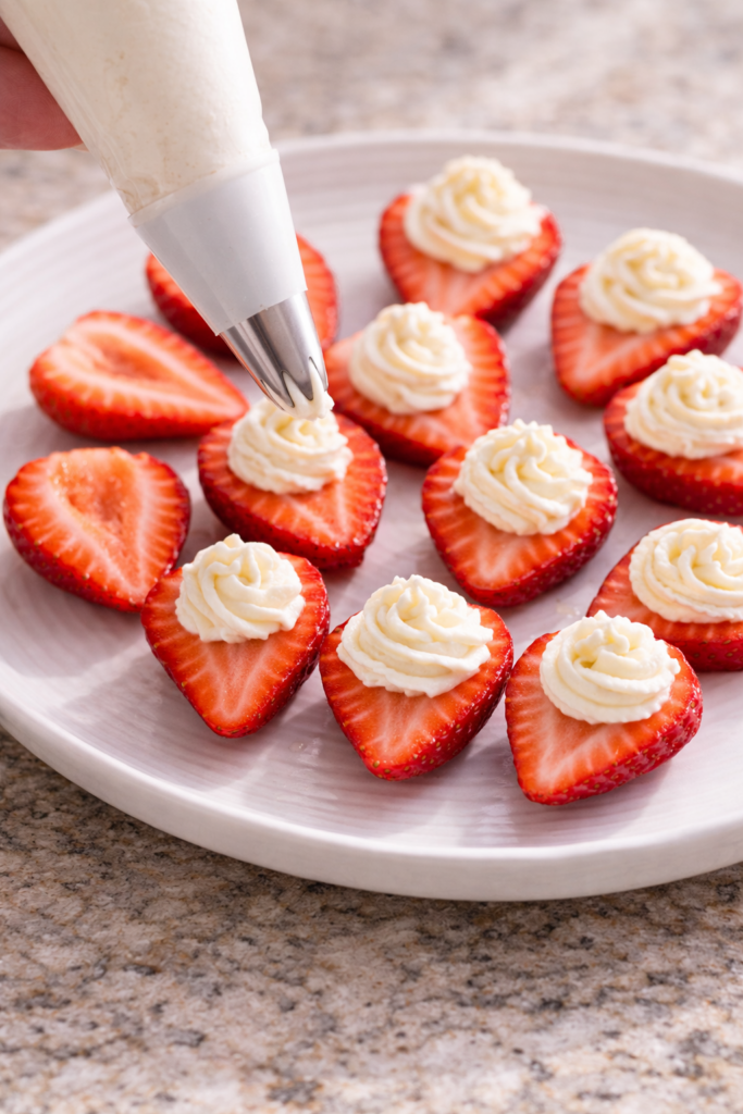 piping cream cheese filling into sliced strawberries
