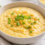 Slow cooker cheesy grits in a bowl topped with shredded cheese and green onions