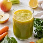fresh apple carrot green juice with apples, lemon, carrots, kale, spinach, and celery on marble countertop