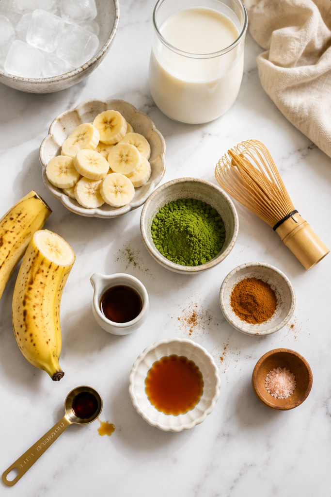 Ingredients for a banana bread matcha latte including sliced banana, milk, matcha powder, cinnamon, maple syrup, and ice.