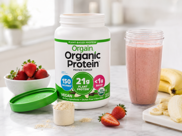 Open tub of Orgain Organic Protein powder on a bright marble kitchen counter with a strawberry smoothie, scoop of protein powder, strawberries, bananas, and the green lid nearby.