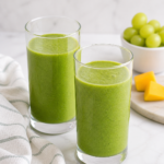 two green smoothies in tall glasses on marble countertop