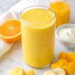 bright sunshine smoothie made with orange juice, pineapple, mango, banana, and creamy yogurt on countertop.
