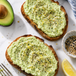 Avocado cottage cheese toast on sourdough with everything bagel seasoning, lemon zest, avocado, and lemon.