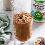 Chocolate protein smoothie with almond butter in a fluted glass topped with sliced almonds and mini chocolate chips.