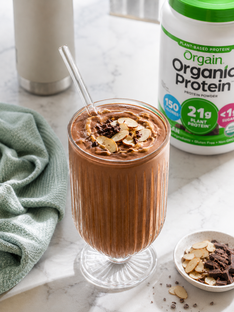 Chocolate protein smoothie with almond butter in a fluted glass topped with sliced almonds and mini chocolate chips.