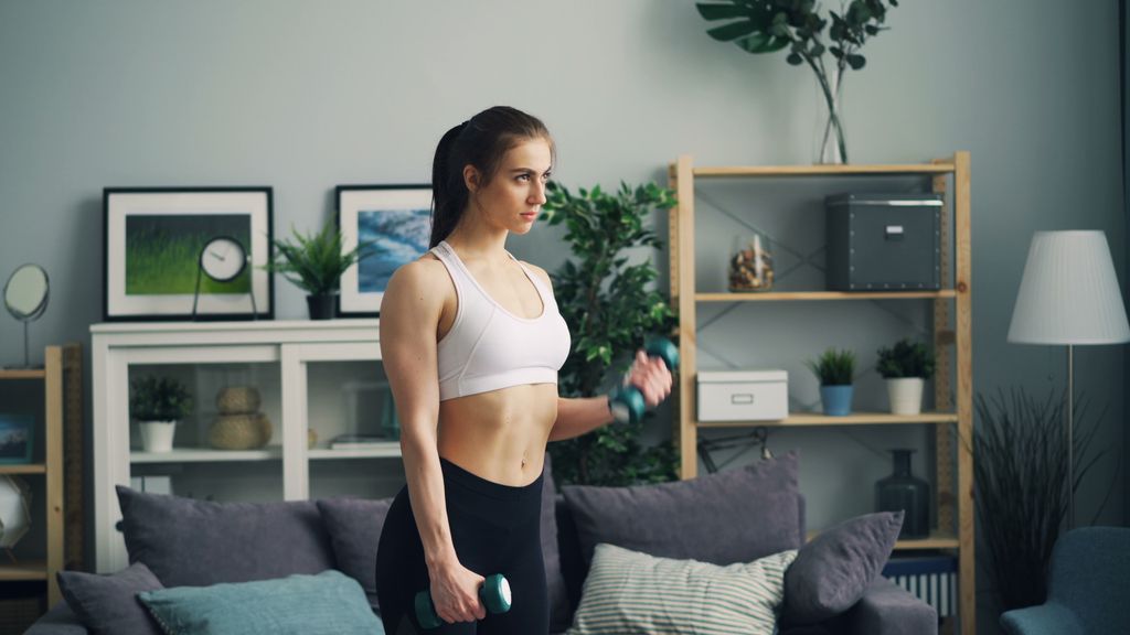 Fit woman in sportswear working out with dumbbells indoors.