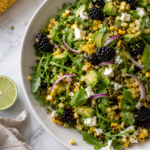 Grilled corn salad with blackberries, avocado, arugula, red onion and crumbled feta in an off-white serving bowl.