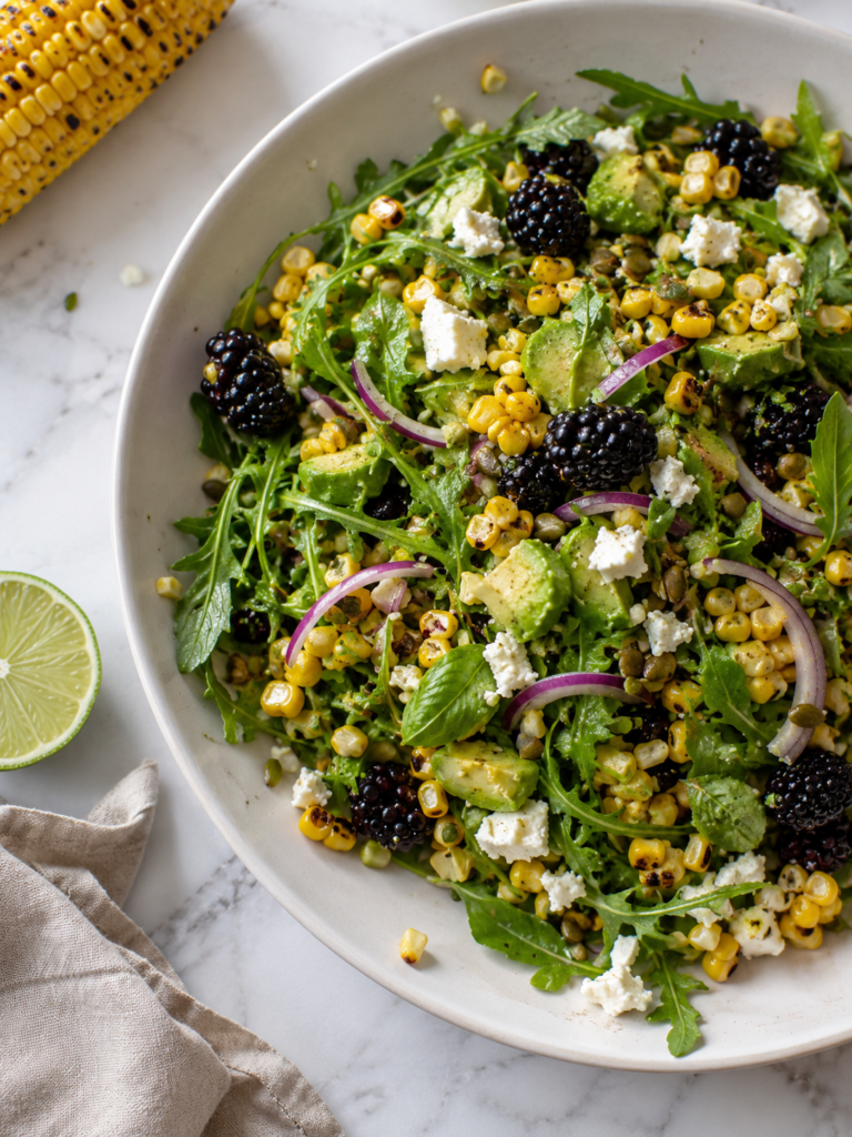 Grilled corn salad with blackberries, avocado, arugula, red onion and crumbled feta in an off-white serving bowl.