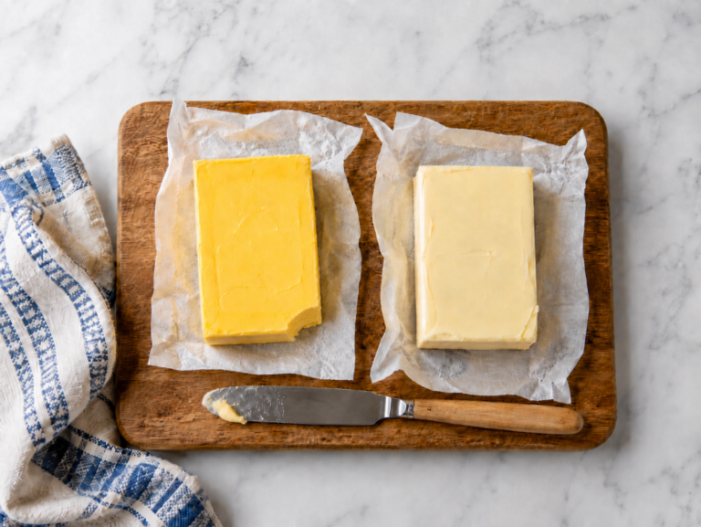 Rich yellow grass-fed butter beside paler conventional butter on a wooden cutting board with a butter knife.