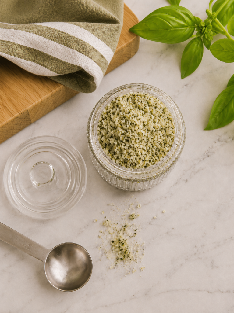 Overhead close-up of homemade basil salt in a ribbed glass jar showing the coarse salt texture and green basil flecks.