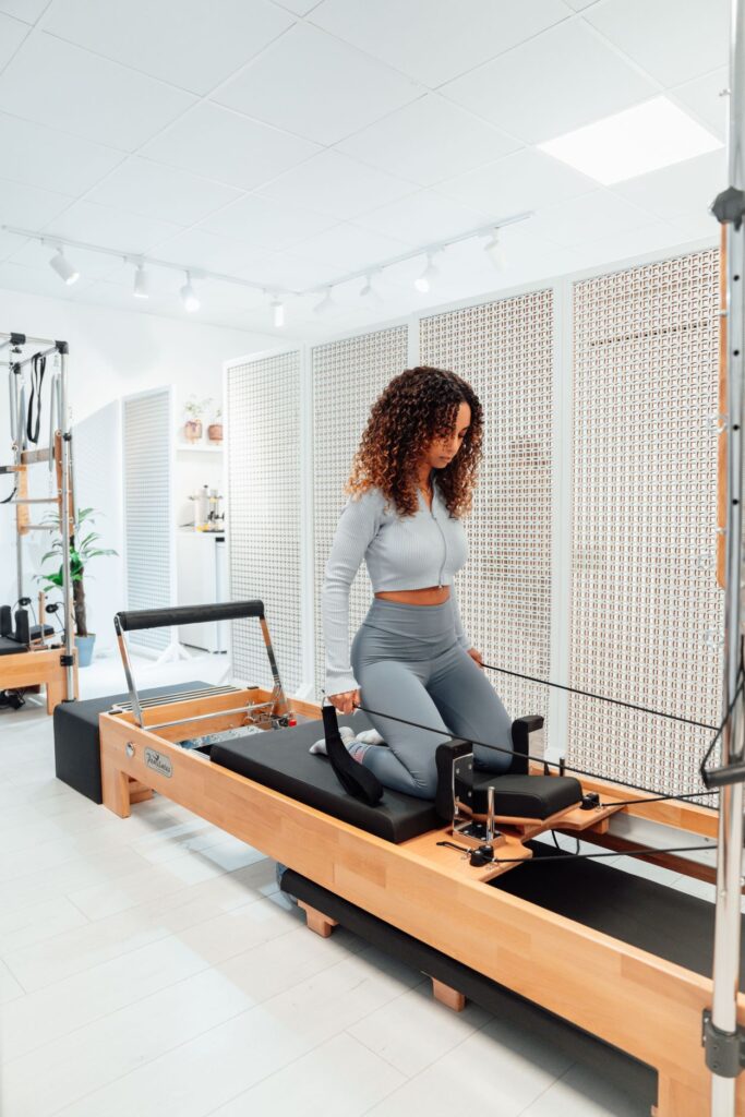 Woman kneeling on a Pilates reformer while using resistance straps