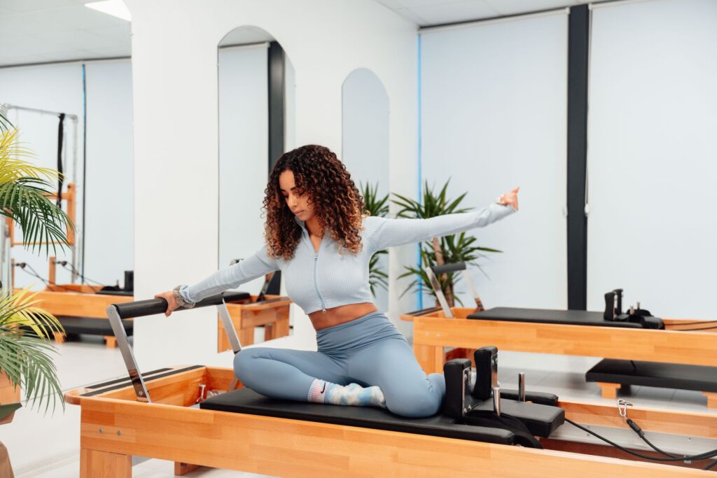 Woman performing a seated side stretch on a Pilates reformer in a bright studio