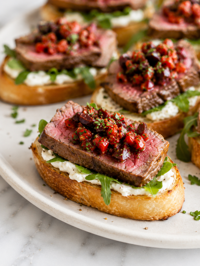 Close-up of steak crostini topped with goat cheese, arugula and roasted red pepper olive relish.