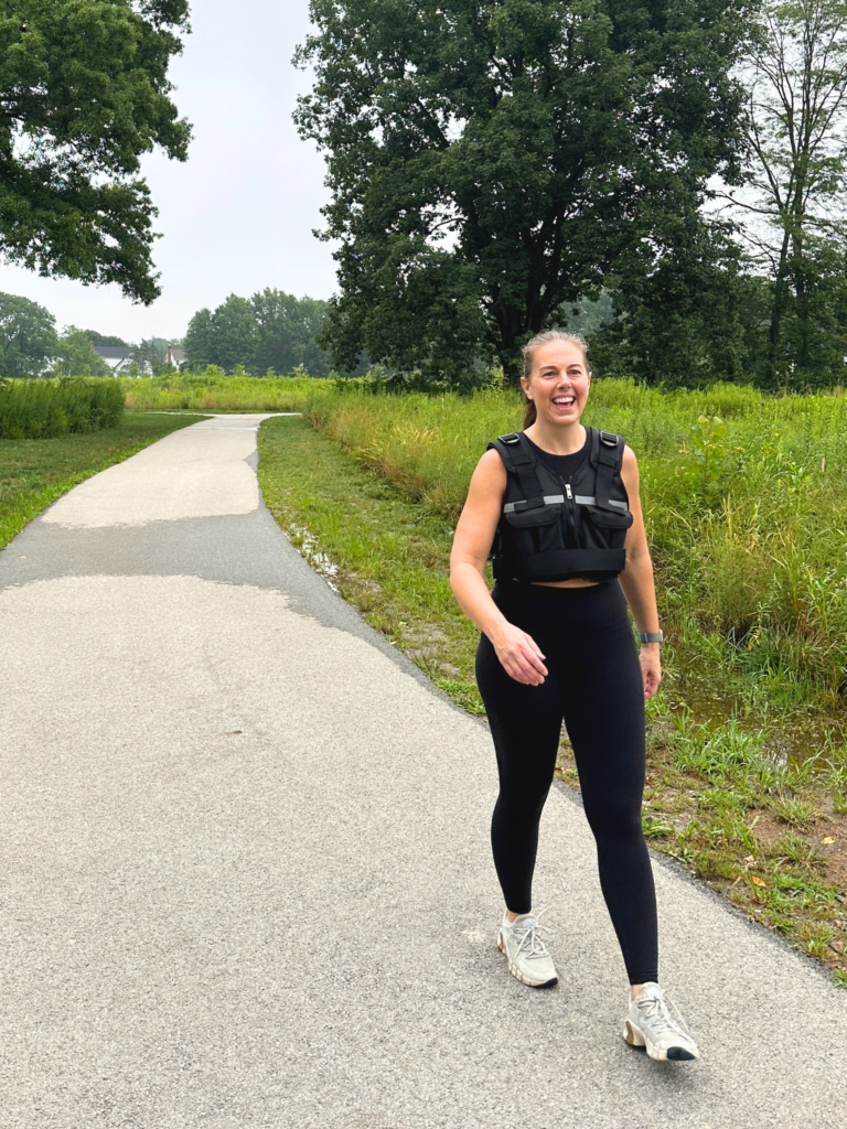 Woman walking on a paved outdoor trail while wearing a black weighted vest