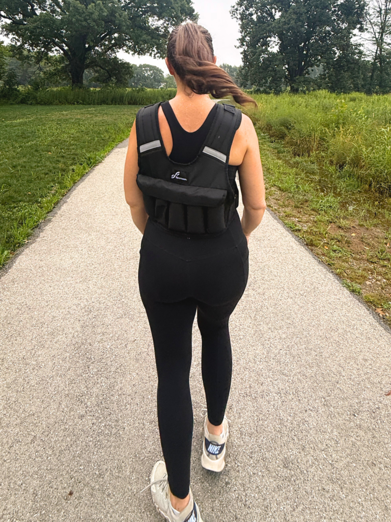 Back view of a black weighted vest worn over workout clothes outdoors