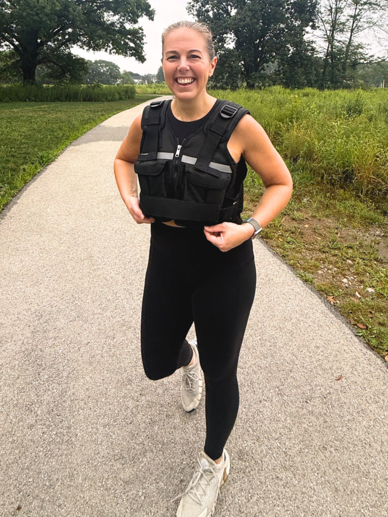 Front view of a woman walking outdoors in a black weighted vest