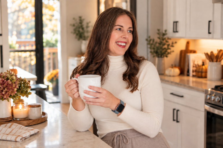 Woman holding a mug of hot coffee in a cozy kitchen during her fall morning routine.