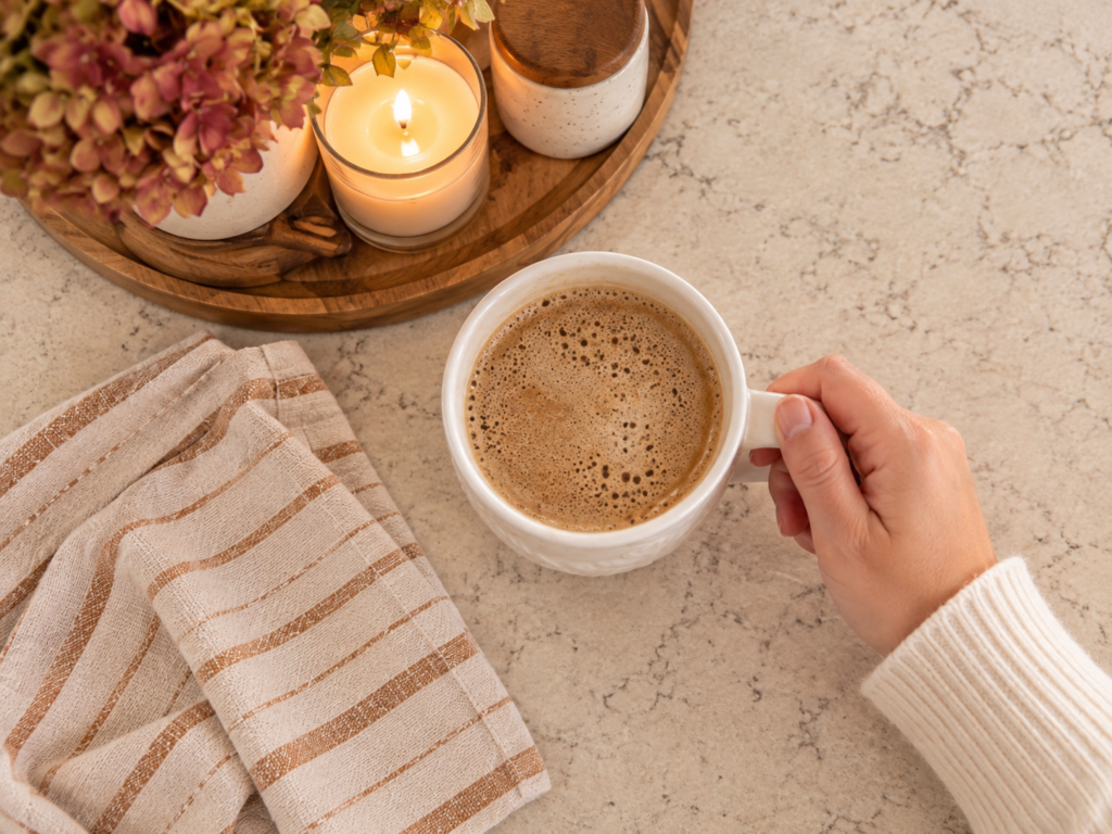 Hot coffee on a kitchen counter with a candle and neutral striped dish towel